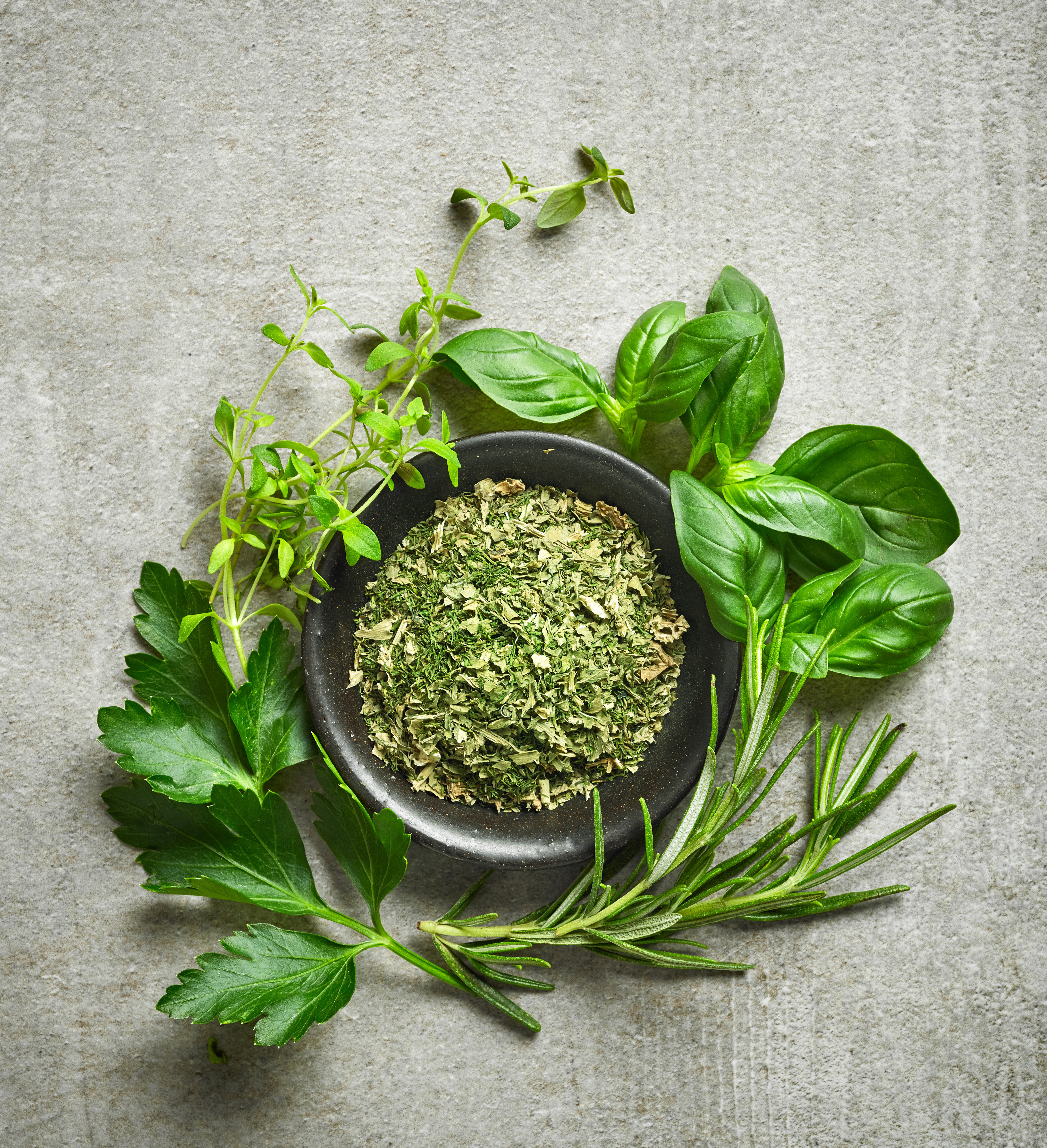 bowl of dried herbs and fresh herbs on gray stone background, top view